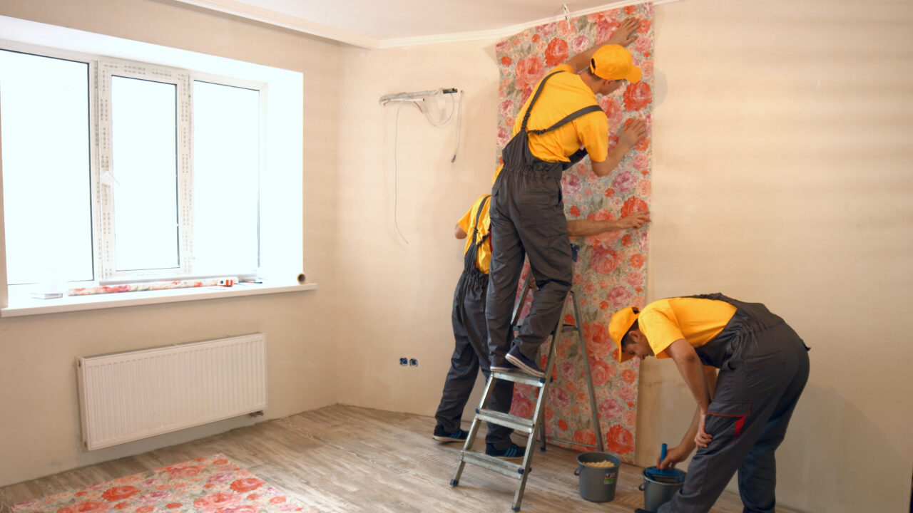 Builders hanging wallpaper in new apartment. Builders working together at construction area.